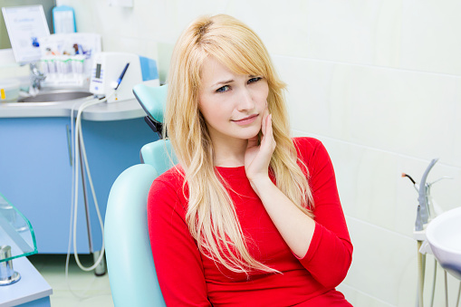 Blonde woman holding her jaw in dental chair