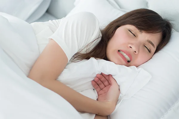 Sleeping woman grinding her teeth in her sleep, likely experiencing bruxism.